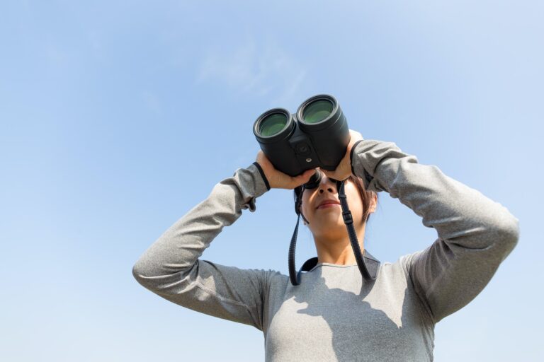 Young Woman looking though binoculars with clear blue sky